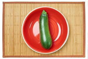 patterned green zucchini squash on a red plate on a cane place mat photo