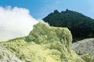 bright smoking fumarole with sulfur deposits against the background of the Mendeleev volcano peak on the island of Kunashir photo