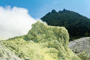 brillante de fumar fumarola con azufre depósitos en contra el antecedentes de el mendeleev volcán pico en el isla de kunashir foto