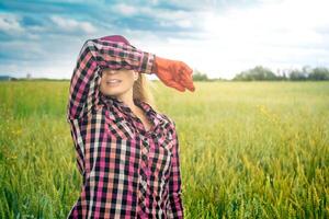 cansado hembra agrícola trabajador en el antecedentes de un campo toallitas el sudor desde su frente con su mano foto