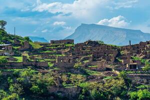 ruins of houses on a mountainside in Kurib, a depopulated village with the only remaining household with an apiary, Dagestan, another village, Chokh, is visible in the distance photo