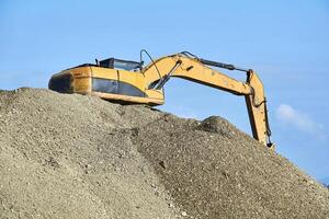 excavator standing on a pile of rubble against the sky photo