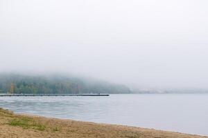 shore of an autumn lake in fog and a pier in the distance photo