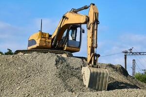 excavator standing on a pile of rubble against the sky and railroad structures photo