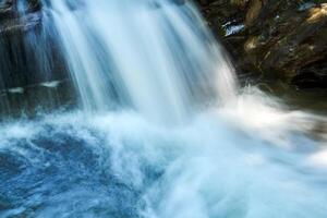 pequeño cascada en un montaña corriente Entre rocas, el agua es borroso en movimiento foto