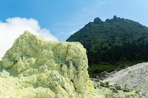 bright smoking fumarole with sulfur deposits against the background of the Mendeleev volcano peak on the island of Kunashir photo