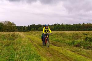 cycling tourist rides on a dirt road through a field photo