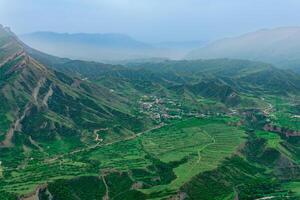 foggy highland valley with vliiage and fields between mountain peaks photo