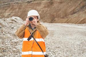 mining or road engineer using a telescope against the background of a mine photo