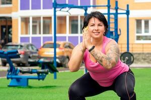 strong plump woman doing squats on a sports ground in the courtyard of a city house photo