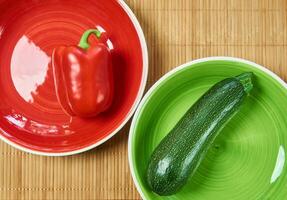 patterned green zucchini squash on a green plate and red bell pepper on a red plate next on a cane place mat photo