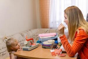 little daughter with a toy sewing machine plays with her seamstress mom photo