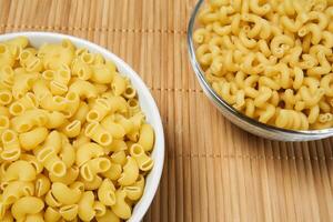 two bowls of dried pasta on a cane tablecloth, close-up photo