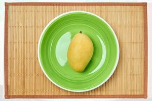 yellow mango on a green plate on a cane place mat photo