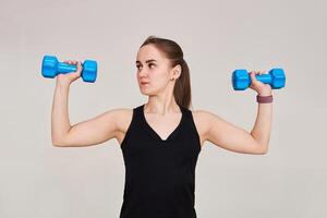 young woman performs an exercise with dumbbells looking to the side, half-length portrait on a light background photo