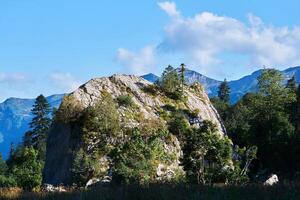 detached huge limestone cliff overgrown with trees against the backdrop of a mountain range photo