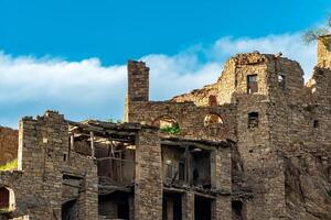 ruins of stone houses attached to the rock in the depopulated village of Gamsutl in Dagestan photo