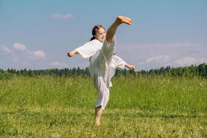 adolescente niña formación kárate kata al aire libre, realiza rotonda patada ushiro mawashi geri foto