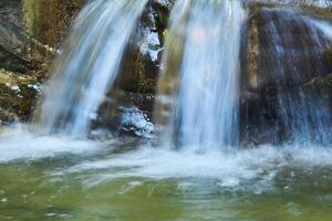 cascada chorros en un montaña corriente Entre rocas, el agua es borroso en movimiento foto