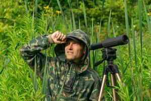 man birdwatcher makes field observation with a spotting scope among the thickets in a river valley photo