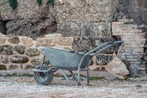 used wheelbarrow against the background of ancient walls at the site of archaeological excavations photo