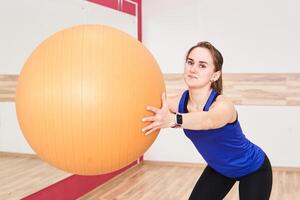 young woman is training by doing squats with exercise ball in gym photo