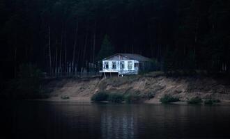abandoned dilapidated house on a dark wooded bank almost collapsed into the river photo