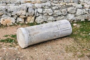 fragment of an antique column with a christian cross carved on it, lying among the ancient ruins photo