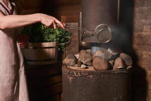 woman in a bath pours water on hot stones on the stove photo