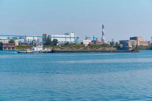 towboat pushes dry bulk cargo barge on the river past the industrial landscape photo