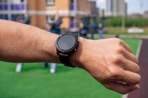 Mira a un reloj inteligente en un del hombre mano en contra el antecedentes de al aire libre ejercicio equipo foto