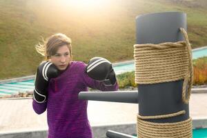 young woman training in combat sport alone on the sports ground with traditional dummies photo