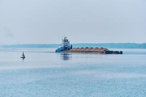 pusher tug pushes dry bulk cargo barge with sand on the river in the morning haze photo