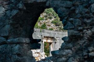 view through a hole in the wall to the entrance portal of ancient temple in the ruins of the antique city of Olympos in Turkey photo