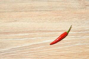 single pod of red chili pepper lies on a wooden surface photo