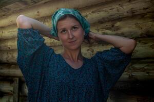 woman in a traditional peasant dress and a headscarf against the background of a log wall photo