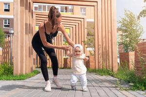 young woman and her toddler daughter walk in the city courtyard, child learns to walk photo