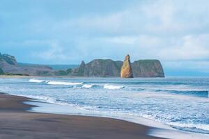 seascape of Kunashir, ocean shore with a huge vertical rock in the water and a quarry among the coastal cliffs photo