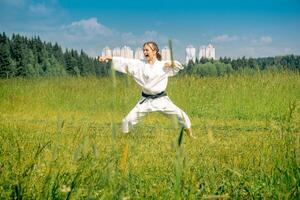 teen girl training karate kata outdoors in the meadow against the background of the city photo