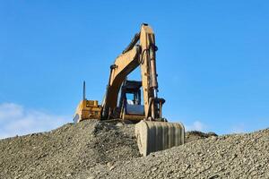 excavator towers on a pile of rubble against the sky photo