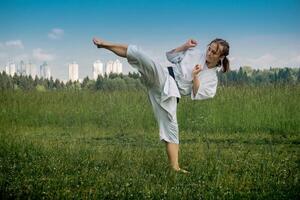 Adolescente niña formación kárate kata al aire libre, realiza el uro mawashi geri gancho patada foto