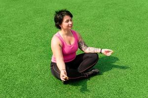 joven robusto gordito mujer medita en el césped después hacer ejercicio foto