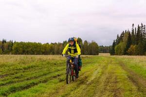 cyclist hiker rides on a dirt road through a field photo