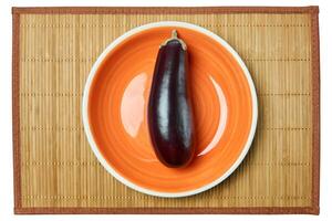 purple eggplant on a orange plate on a cane serving mat photo