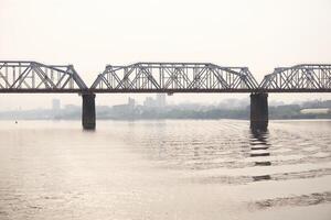 road bridge over a wide river and the silhouette of a distant city behind it in the morning fog photo