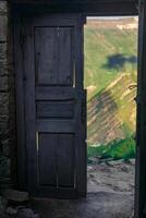 wooden door in the ruins of an abandoned house through which mountains are visible, in the ruins of the ghost village of Gamsutl in Dagestan photo