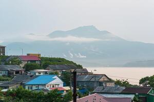 landscape of the town of Yuzhno-Kurilsk on the island of Kunashir with a view of the sea bay and the Mendeleev volcano in the distance photo