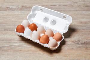 eggs of different colors from white to brown together in a crate on a wooden table surface photo