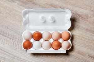 eggs of different colors from white to brown together in a crate on a wooden table surface photo