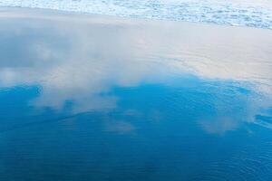 ocean beach with a wave coming back, in which the sky is reflected photo